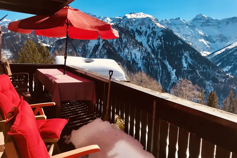 Het balkon met rode parasol en stoelen, besneeuwde bergen erachter