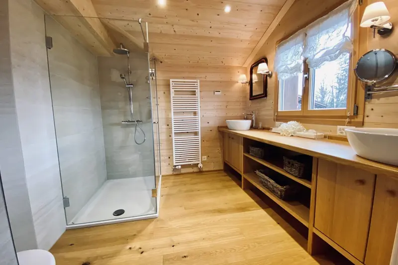 Badkamer met douche en twee wastafels op een houten meubel