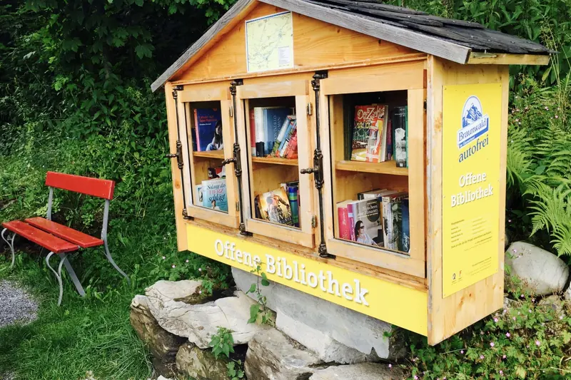 Een open boekenkast en een rood bankje langs de weg