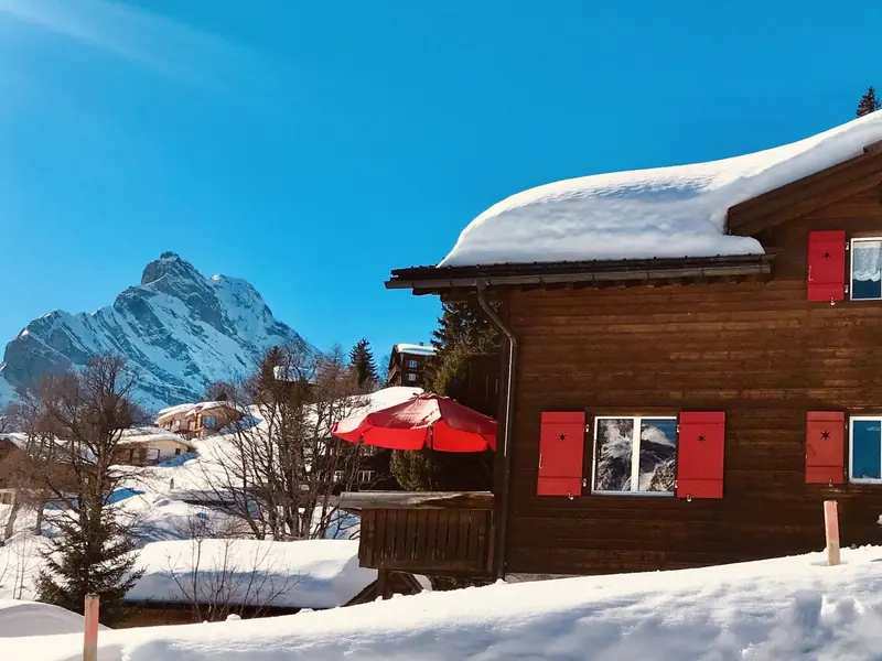 Chalet Heidi in de sneeuw, met rode luiken en een rode parasol