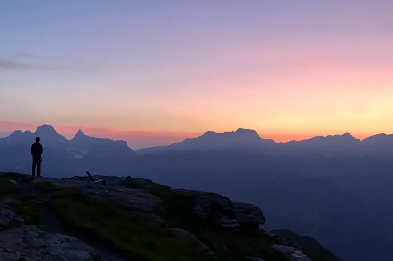 Roze lucht boven de bergkammen, iemand op een rotsrand