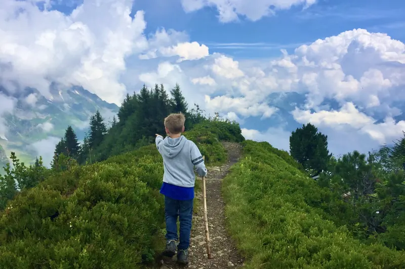 Een jongen met wandelstok wijst naar de wolken