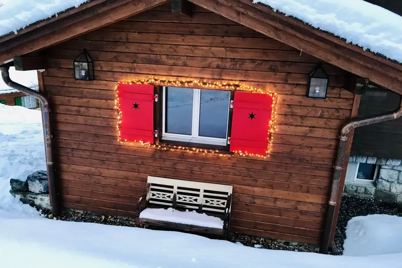 Rode luiken met lichtjes en een bankje in de sneeuw